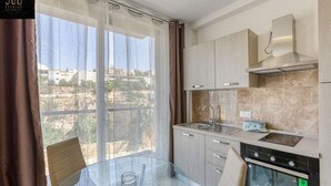 A modern kitchen with a glass dining table, a stove, and a view of the city through large windows. - Cozy 1BR home in the centre of St Julians w/WIFI (San Ġiljan)