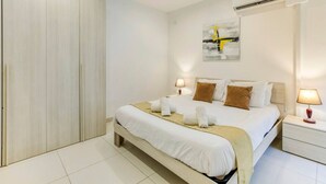 Un dormitorio moderno con una cama grande, dos mesitas de noche con lámparas, un armario y un cuadro en la pared.