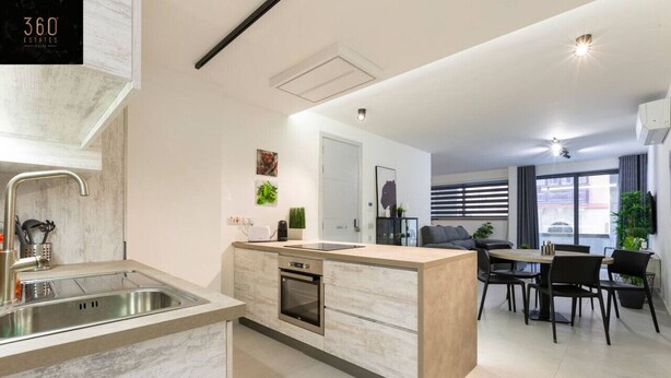 A modern kitchen with a built-in oven, a sink, and a dining area with a table and chairs.