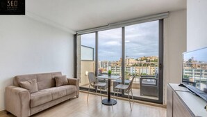 A modern apartment with a large window, a sofa, a dining table, and a TV.