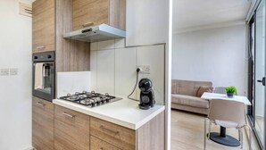 A modern kitchen with a gas stove, oven, and coffee maker, and a small dining area with a table and chair.
