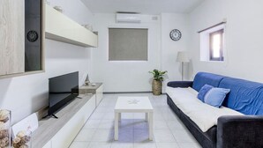 A modern living room with a flat-screen TV, a sofa, a coffee table, and a window with a view. - Peaceful 1BR maisonette with Sofa Bed with WIFI ! (San Pawl il-Baħar)