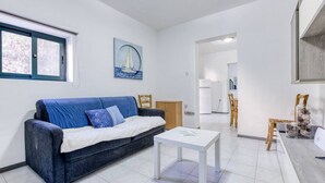 A living room with a blue sofa, a white coffee table, and a painting of a sailboat. - Peaceful 1BR maisonette with Sofa Bed with WIFI ! (San Pawl il-Baħar)
