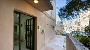 A building entrance with a glass door, a small outdoor seating area, and a paved pathway. - Peaceful 1BR maisonette with Sofa Bed with WIFI ! (San Pawl il-Baħar)