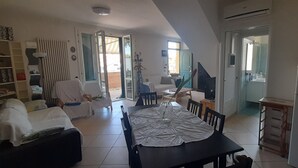 Un salon spacieux comprenant une table à manger, un canapé et des fauteuils. Il y a également un coin cuisine équipé d’un réfrigérateur et d’un four à micro-ondes.