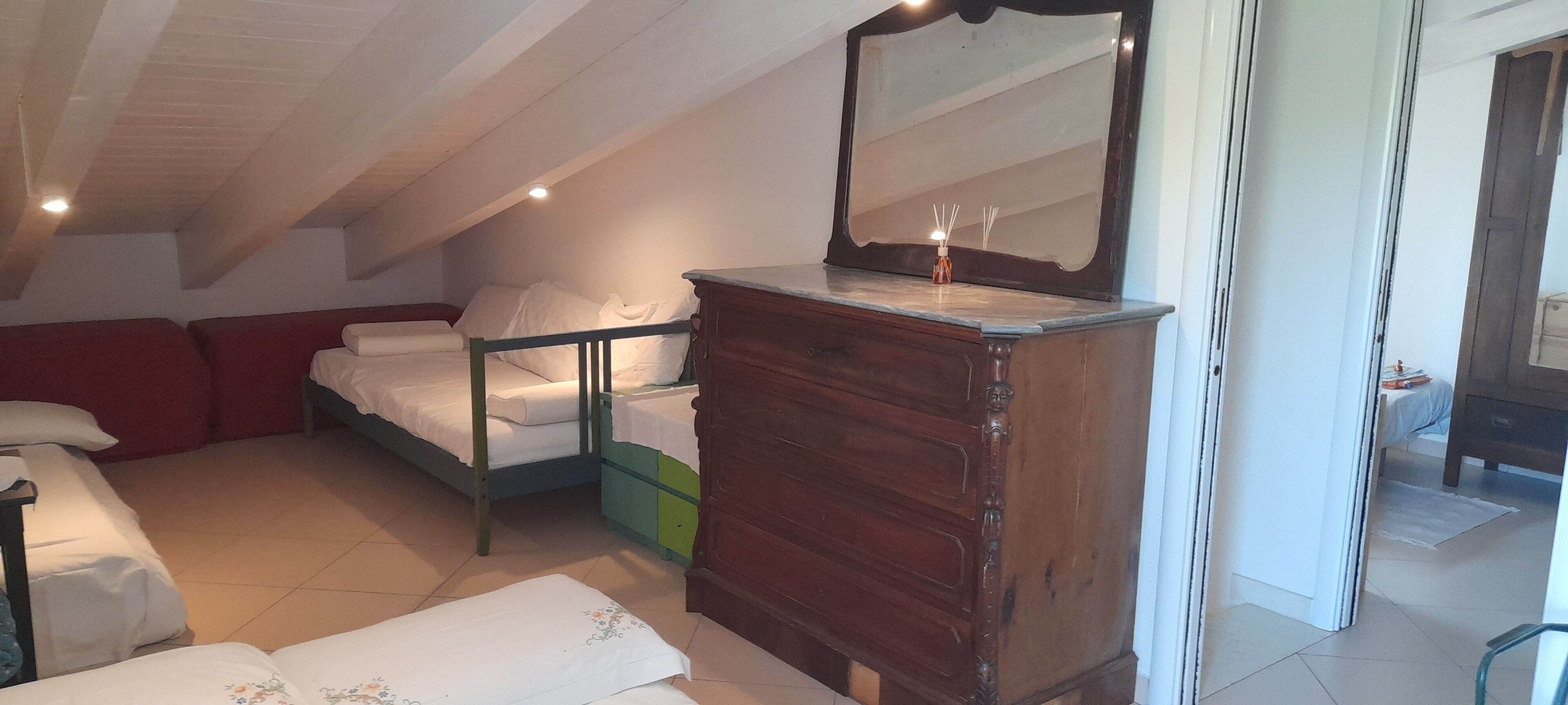 Een slaapkamer met een houten dressoir, een bed met witte lakens, een groene opbergkast en een grote spiegel.