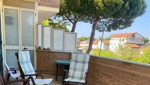 Un balcon avec deux chaises en bois, une petite table et un tonneau bleu.