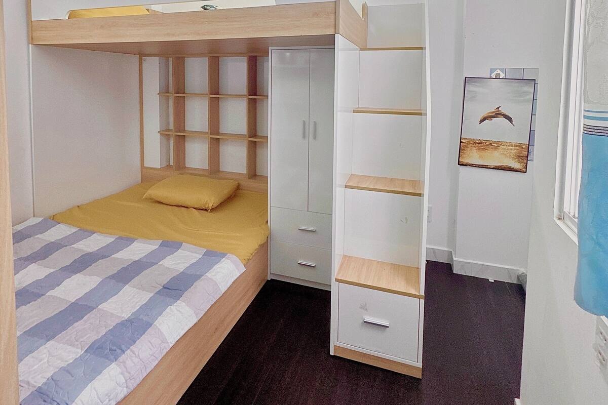 A bunk bed with a wooden frame and a yellow pillow, a white wardrobe with multiple drawers, and a ceiling fan.