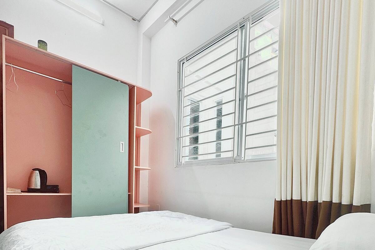 A hotel room with two beds, a wardrobe, a window with blinds, and a curtain.