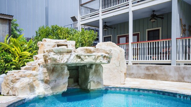 A swimming pool with a rock feature, surrounded by a building with a balcony and a fence.