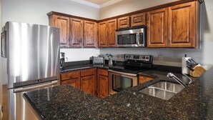 A kitchen with wooden cabinets, stainless steel appliances, granite countertops, and a stainless steel sink.
