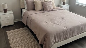 Un dormitorio con una cama, dos mesitas de noche, una mesilla auxiliar, una alfombra estampada y una ventana.