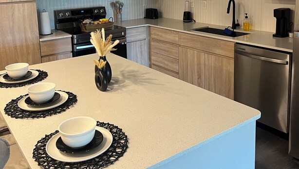 Una cocina moderna con una isla central, lámparas colgantes blanco y negro, microondas, estufa y lavavajillas.