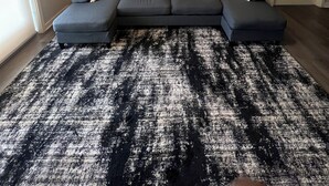 Una sala de estar con un sofá seccional, un tapete estampado, un ventilador de techo y una obra de arte colgada en la pared.