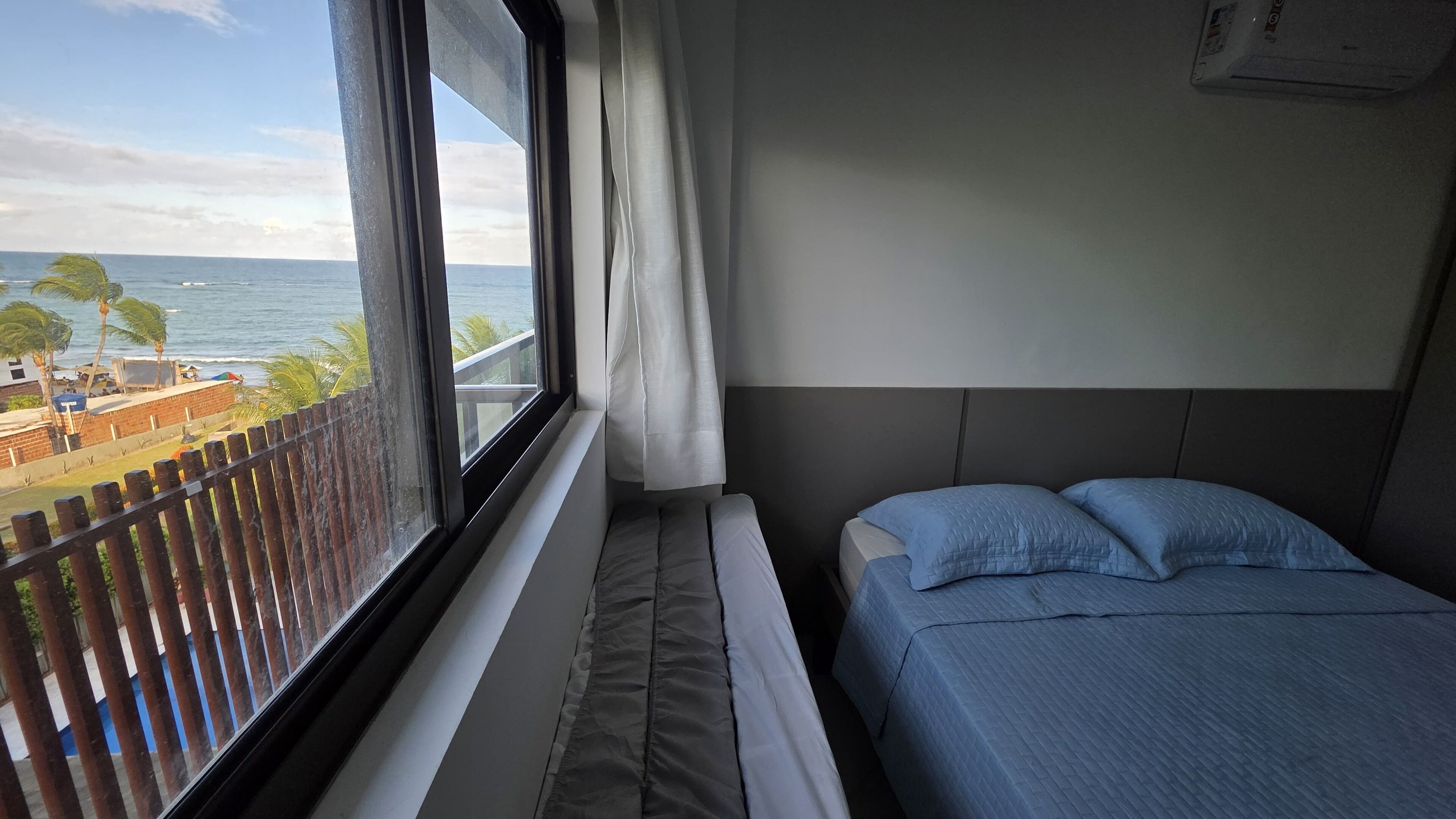 A hotel room with a bed, a window with curtains, and a view of the beach and ocean.