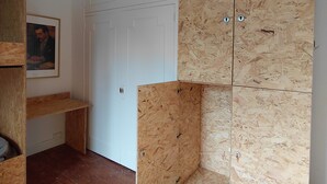 A room with a wooden floor, a white door, and a wooden cabinet with a picture on the wall.