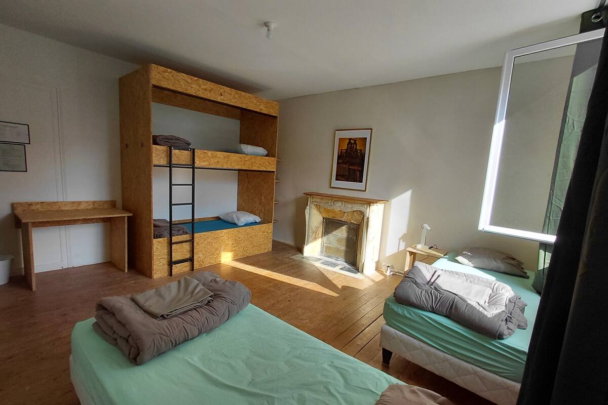 Een kamer met stapelbedden, een bureau, een open haard en een bed met kussens.