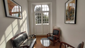 A room with a wooden floor, a sofa, a chair, a small table, and a large window with a view of trees.