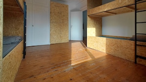 A room with wooden flooring, bunk beds, and a white door.