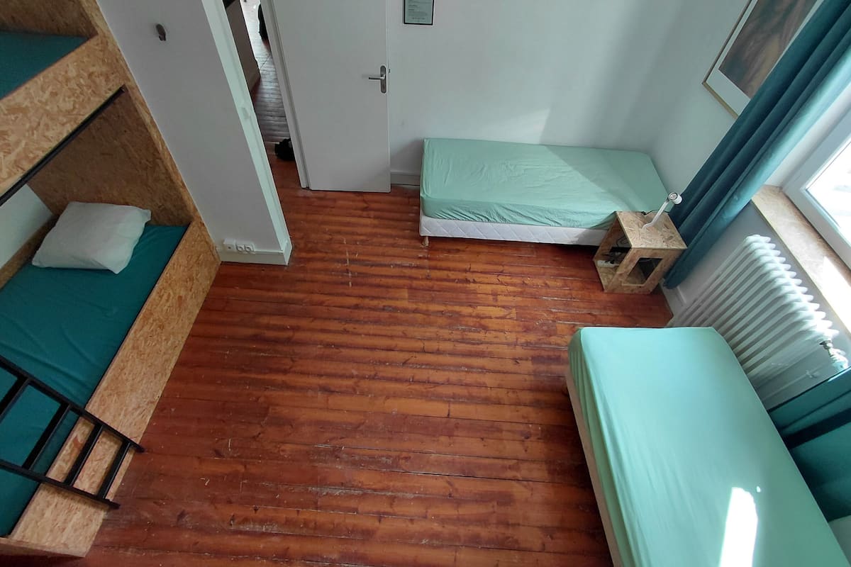 Een slaapzaal met stapelbedden, een enkel bed, een radiator en een raam met gordijnen.