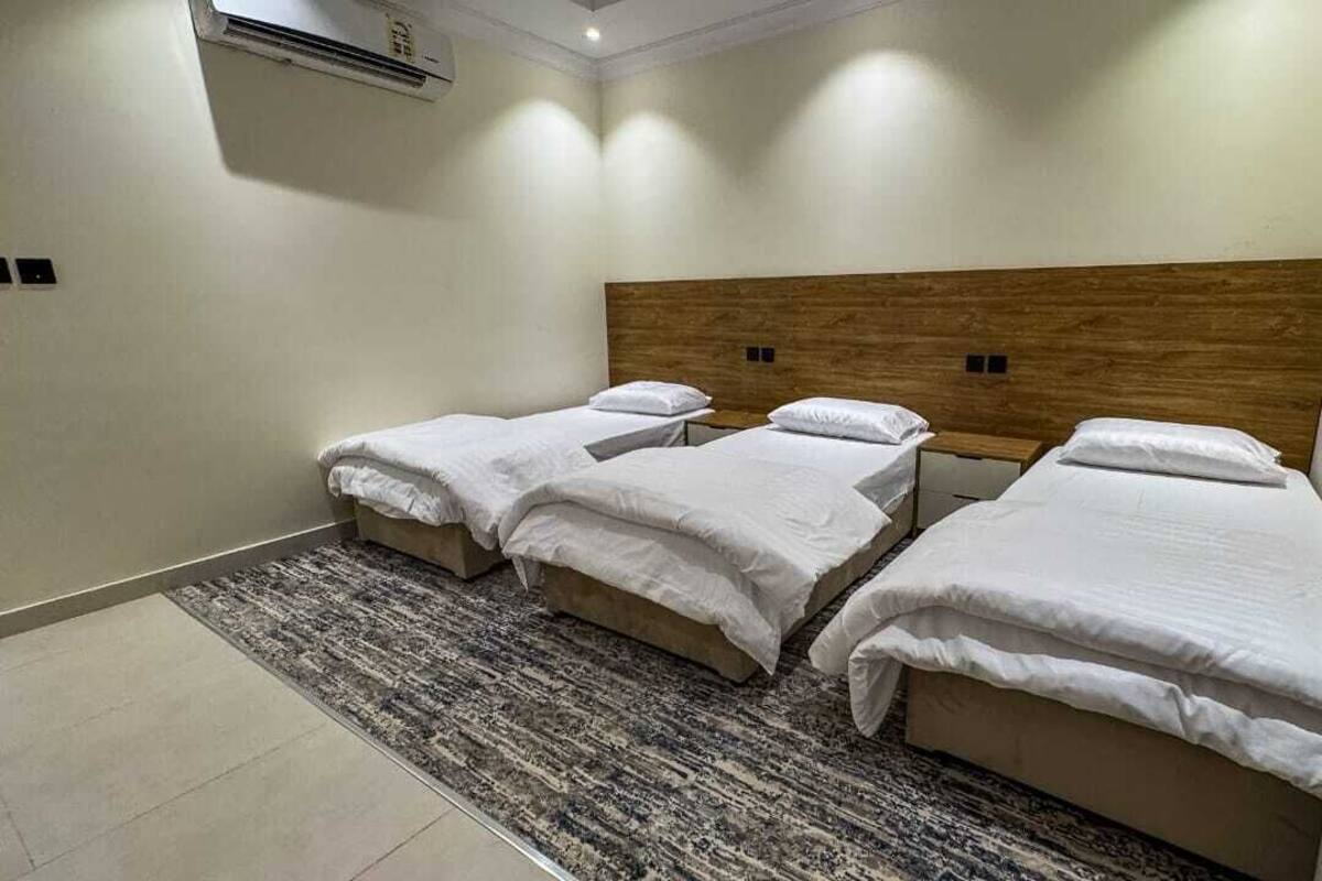 A hotel room with three single beds, a wooden headboard, a patterned rug, and an air conditioning unit.