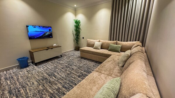 Una sala de estar moderna con un sofá modular, un televisor de pantalla plana, una pequeña consola, una planta en maceta y una alfombra estampada.