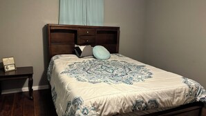A bedroom with a bed, wooden headboard, a nightstand, and a light blue curtain. - Entire Home  4-bedroom house in LakeWhitney Estates with WiFi, AC. Book now! (Whitney)