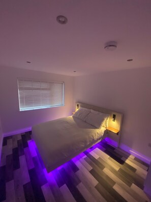 Een slaapkamer met een bed, een raam met zonwering en een vloer met patroon.