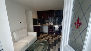A modern living room with a glass coffee table, a white sofa, and a kitchen in the background. - Stunning Truro 1-bed - Sleeps 2 & Parking (Truro)
