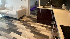 A modern kitchen with a central island, dark wooden flooring, and a white sofa in a living area. - Stunning Truro 1-bed - Sleeps 2 & Parking (Truro)
