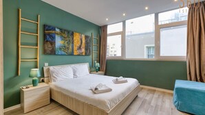 Un dormitorio moderno con una cama grande, una mesita de noche, un sofá azul y una ventana con cortinas.