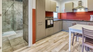Una cocina moderna con cabina de ducha de vidrio, suelo de madera y zona de comedor con mesa y sillas.