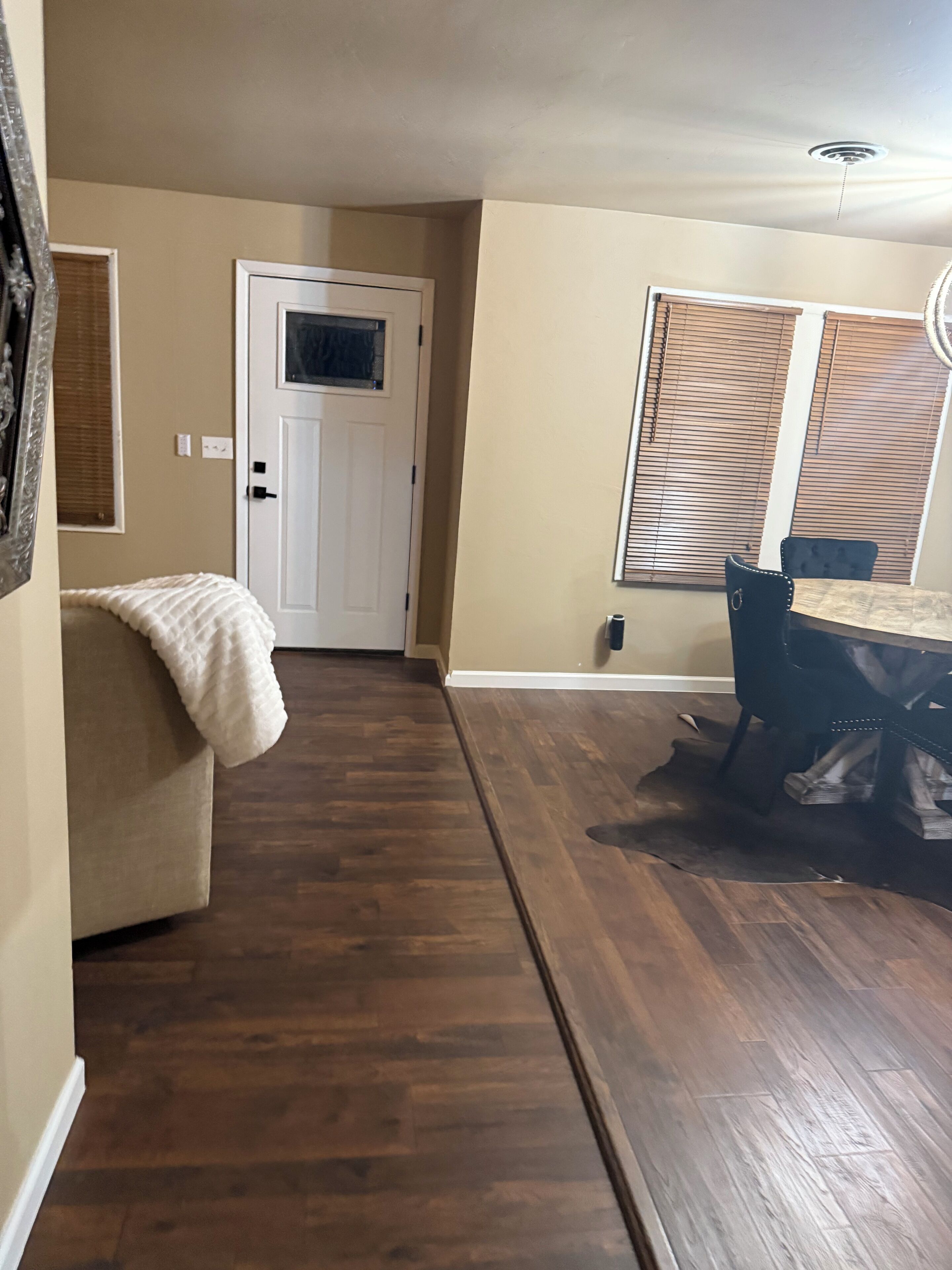 Un couloir avec un plancher en bois, une porte blanche et un coin repas comprenant une table et des chaises.