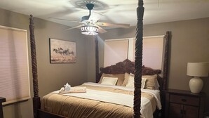 Un lit à baldaquin avec des poteaux aux quatre coins, un ventilateur de plafond, une lampe de chevet et un tableau encadré au mur.