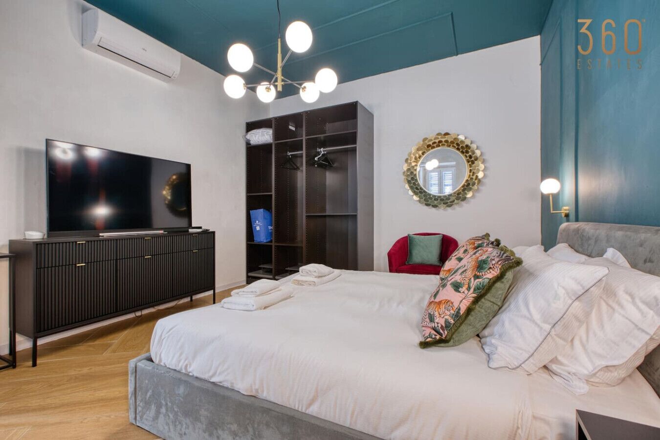 Une chambre moderne avec un grand lit, une télévision, une armoire et un miroir.