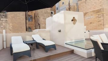 Une terrasse sur le toit, avec des chaises longues, une table en verre et un parasol noir.