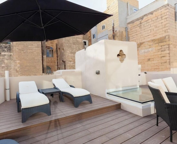 Una terraza en la azotea con sillones de descanso, una mesa de vidrio y un paraguas negro.
