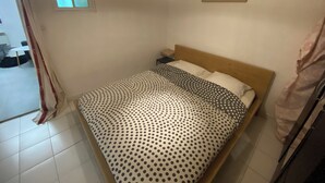 A bedroom with a bed, a nightstand, a window with curtains, a wall-mounted picture, and a hanging light fixture.