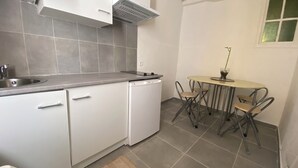 A compact kitchen with white cabinets, a built-in dishwasher, a small dining table with four chairs, and a window with a view.