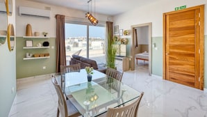 Una sala de estar moderna con una mesa de comedor de vidrio, un sofá y un ventanal con vistas a la ciudad.