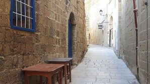 Une ruelle étroite aux murs de pierre, avec un banc en bois et une petite table.