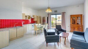 Un appartement moderne comprenant une cuisine, un coin repas et un salon. Il est doté d’un crédence en carreaux rouges, de meubles de cuisine en bois et d’une grande fenêtre offrant une vue dégagée.