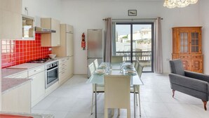 Une cuisine moderne avec des meubles blancs, un dosseret carrelé de carreaux rouges et un coin repas comprenant une table et des chaises en verre.