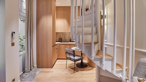 A modern kitchen with wooden cabinets, a dining area with a table and chairs, and a staircase with white railings. - Stunning AC Duplex Apartment - Champs Elysees (Paris)