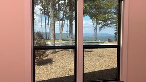 A room with a large window overlooking a grassy area with trees and a view of the sea.