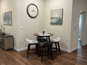Un comedor con una mesa redonda, dos sillas, un reloj y obras de arte en las paredes.