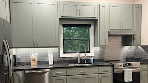 A modern kitchen with grey cabinets, stainless steel appliances, and a window providing natural light.