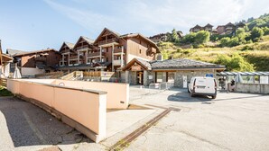 A multi-story hotel with a wooden facade, a covered entrance, and a parking area. - Quiet Apartment at the Foot of the Slopes (Valmeinier)