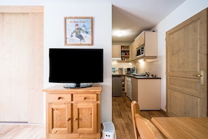 A room with a wooden cabinet, a television, a kitchen with cabinets and a microwave, and a wooden door. - Quiet Apartment at the Foot of the Slopes (Valmeinier)