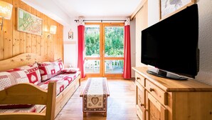 A wooden room with a sofa, a television, and a view through a glass door. - Quiet Apartment at the Foot of the Slopes (Valmeinier)